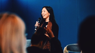 Shae holding a mic and speaking in front of audience