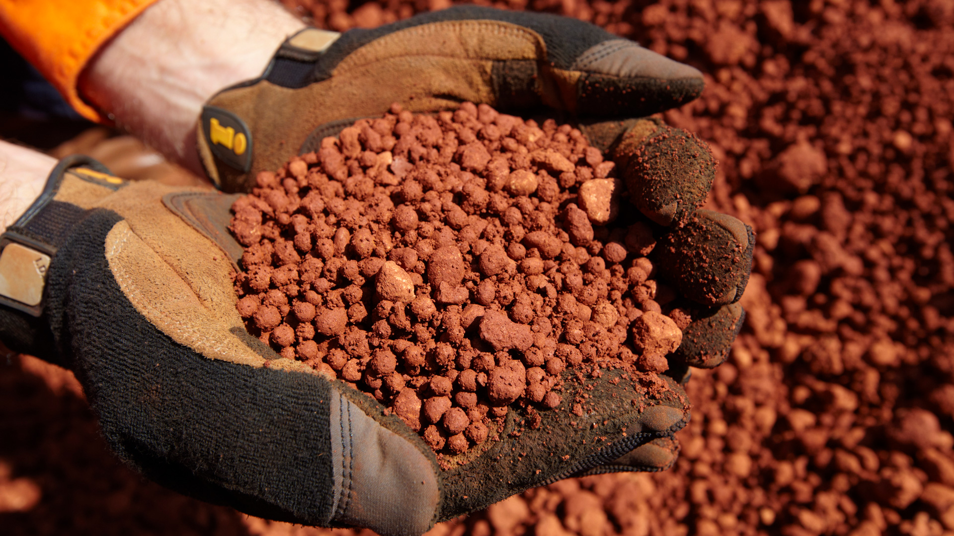 A site worker with gloves holding a handful of bauxite