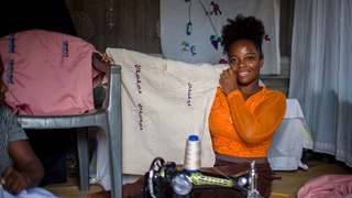 Homzia showing her white piece of cloth crafted creatively behind a sewing machine. 