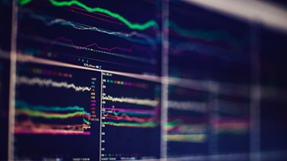 Multiple computer monitors displaying real-time data visualisations with coloured trend lines and performance metrics.