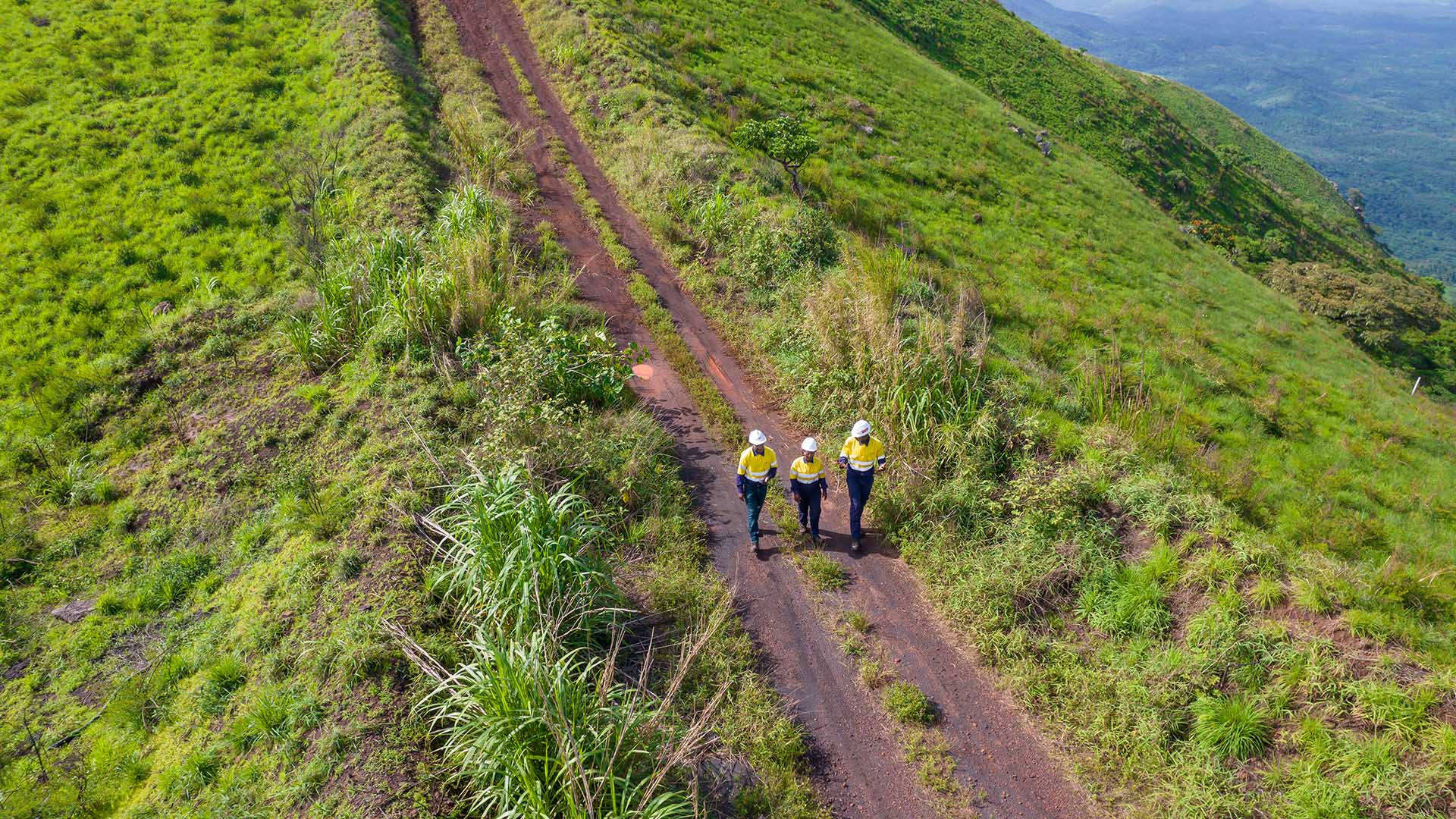 Aerial photo of employees walking along dirt road on mountain ridge above Canga East Camp, Simandou, Guinea