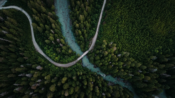 Aerial view of a winding road crossing a turquoise river through dense green forest.